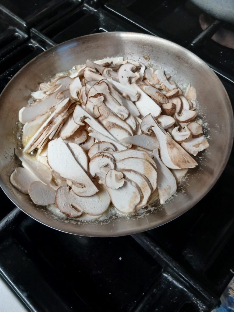 L'immagine mostra una padella sul fornello con all'interno funghi ancora da cuocere